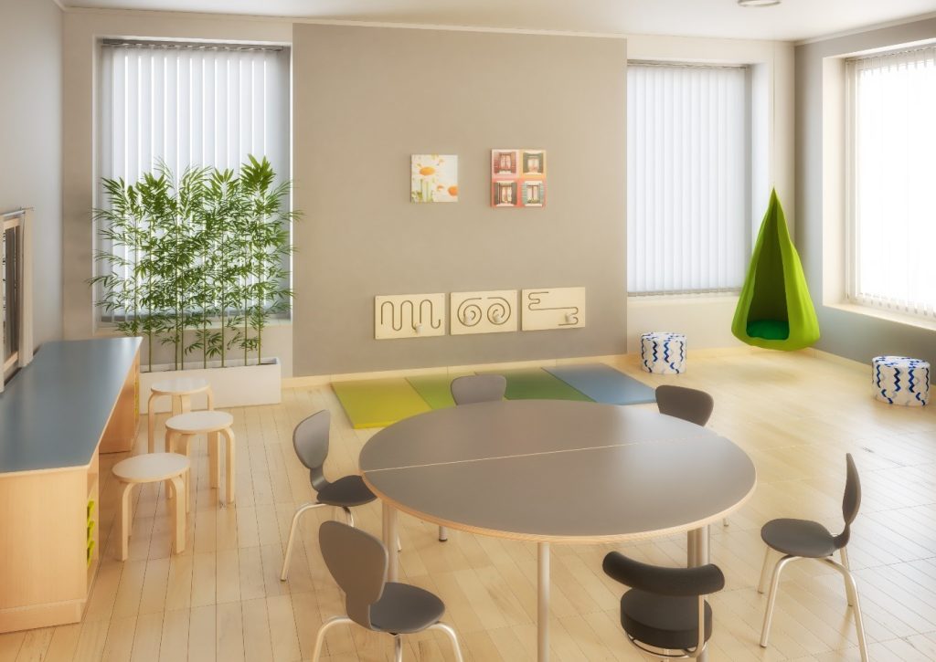 Moderné vybavenie terapeutickej miestnosti – okrúhly stôl, ergonomické stoličky a relaxačná zóna s farebnými podložkami a závesným kreslom pre deti