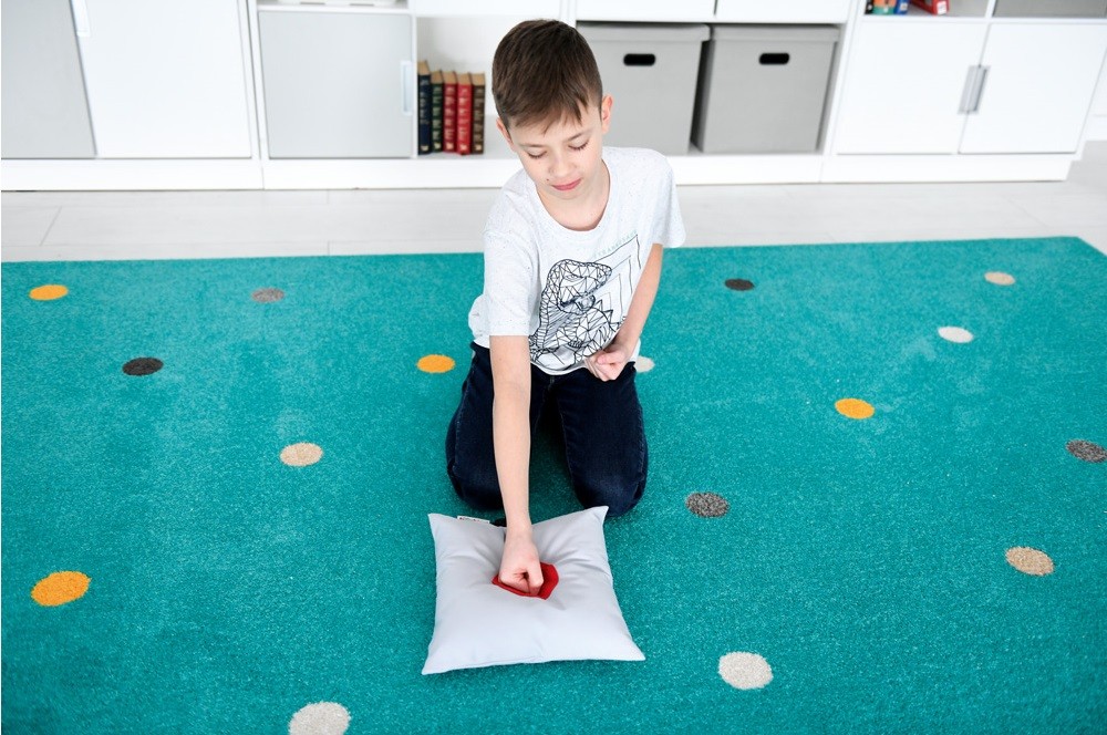 Chlapec pracuje s relaxačnou pomôckou na vankúši v učebni, ktorá podporuje vnímanie a upokojenie počas terapie.