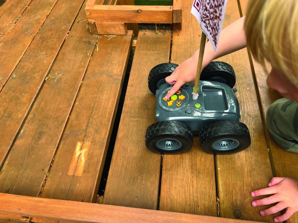 Dítě pohání terénní robot po dřevěné podlaze a zkoumá různé terény, což podporuje jeho motorické a kognitivní dovednosti.