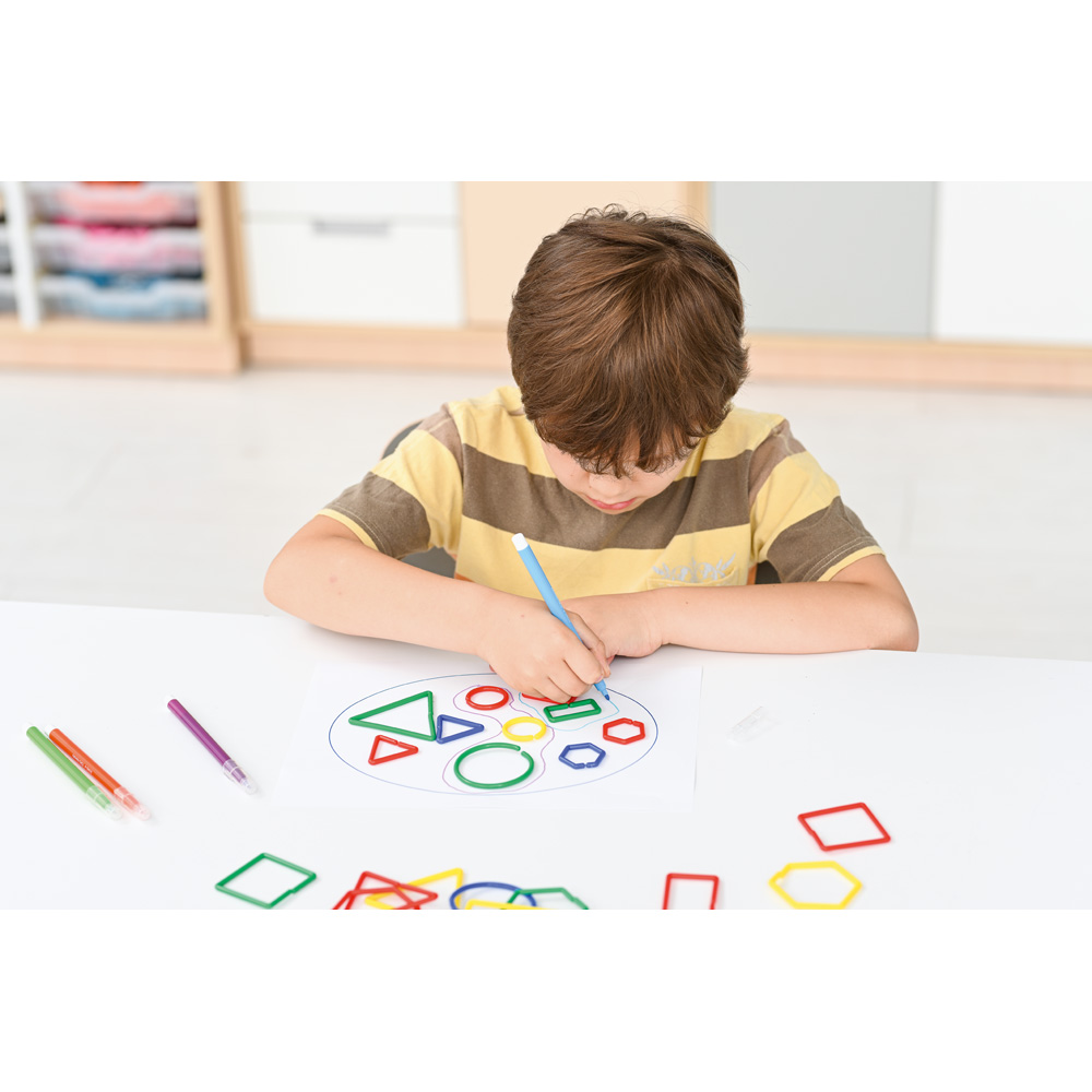 Chlapec kreslí tvary na papier, okolo má rozložené farebné geometrické tvary.