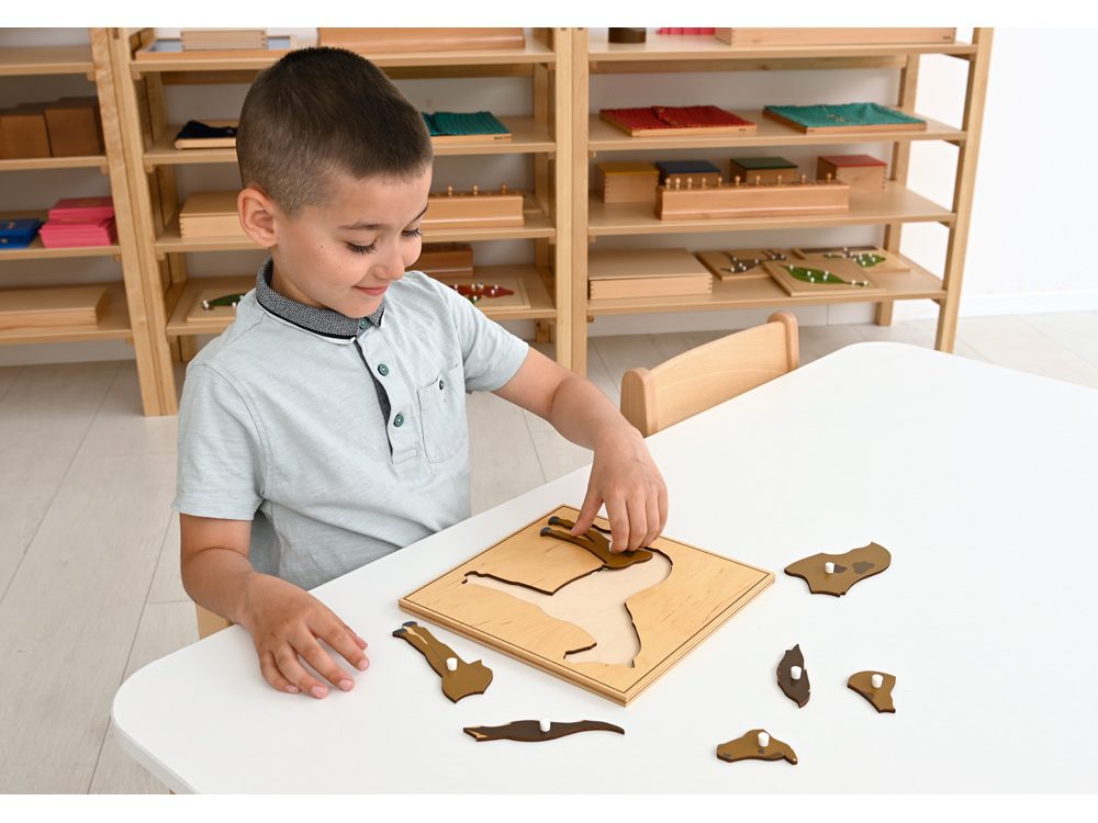 Malý chlapec sedí pri stole a skladá drevené edukačné puzzle v svetlej triede.