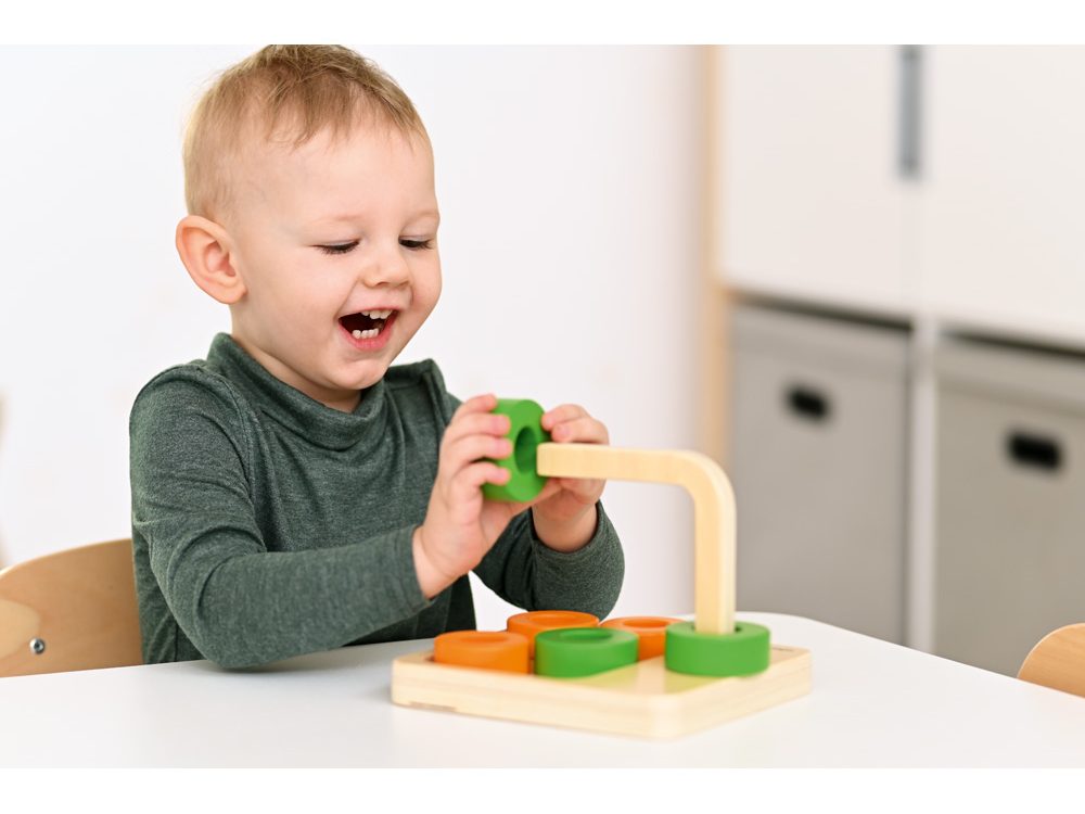 Dieťa sa usmieva pri hre s montessori didaktickou hračkou podporujúcou samostatnosť a logické myslenie