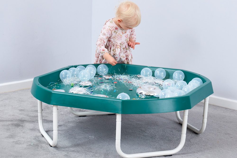 Malé dieťa objavuje rôzne materiály v senzorickom stole naplnenom balónikmi, fóliou a drobnými predmetmi