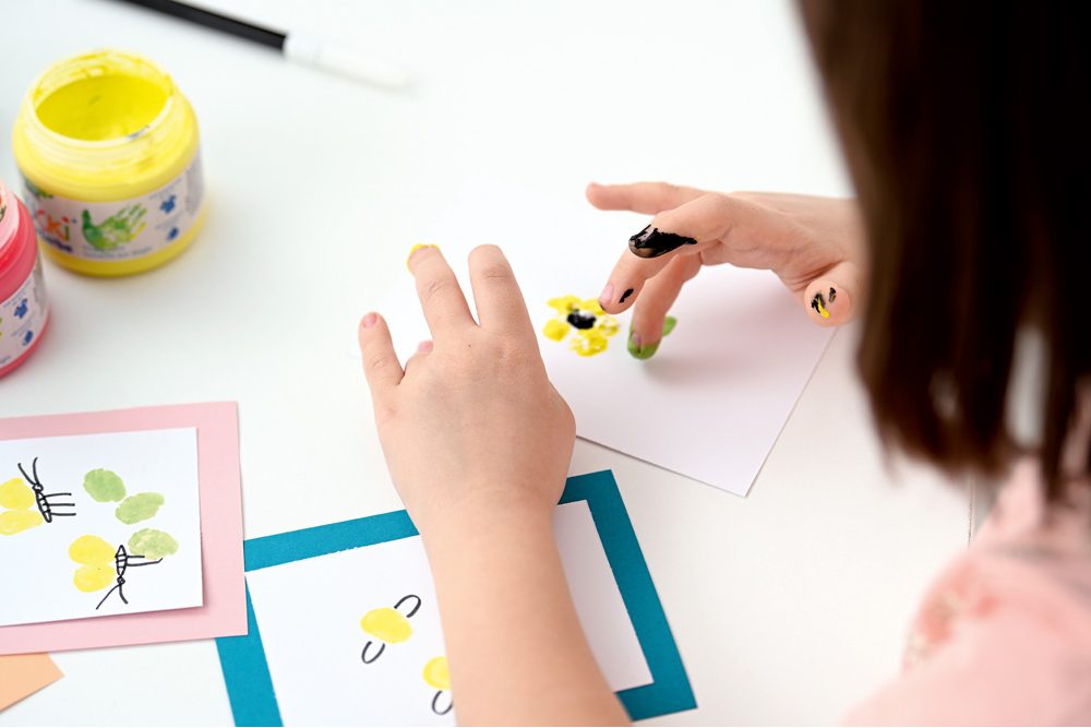 Dieťa maľuje prstami farebnými farbami na papier a rozvíja kreativitu aj hmatové vnímanie