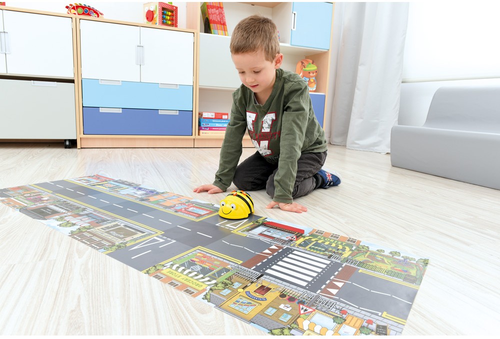Chlapec ovláda Bee-Bot na tematickej podložke s cestami a mestom počas hry v triede.