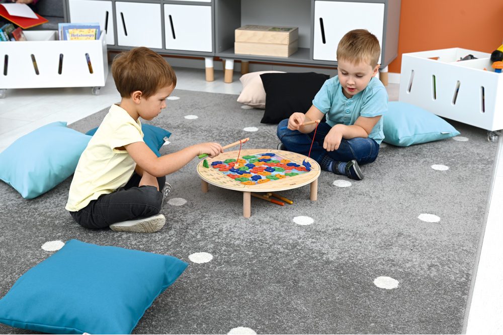 Deti sedia na koberci a lovia farebné rybky pomocou udíc v spoločnej hre.
