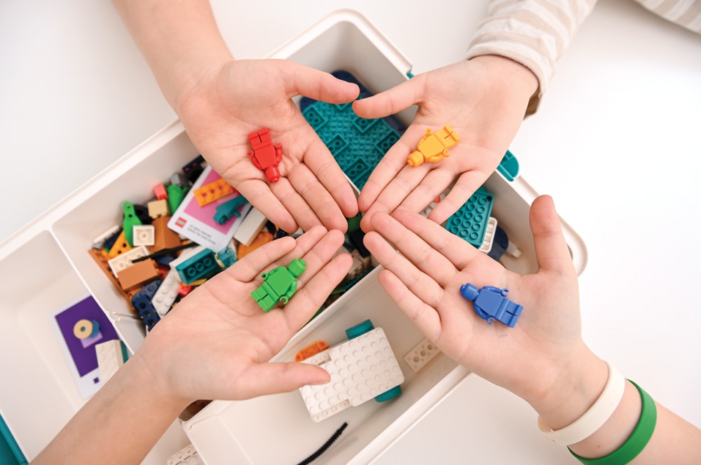 Deti ukazujú LEGO® figúrky rôznych farieb – pripravené na tímovú prácu.